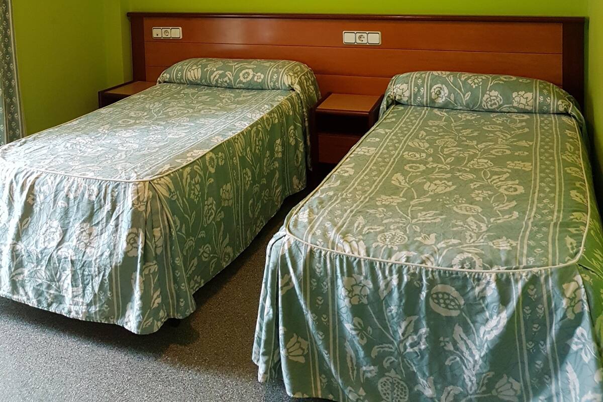 Une chambre avec deux lits simples, une tête de lit en bois, un tableau encadré au mur et une petite table entre les lits.