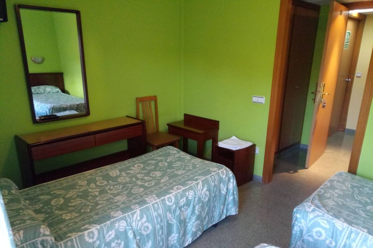 Une chambre avec deux lits, un bureau, une chaise et un miroir, le tout dans une pièce aux murs verts.