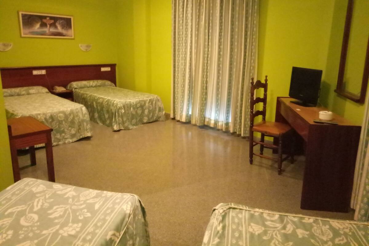 Une chambre d’hôtel avec deux lits simples, un bureau avec une chaise, une télévision et une fenêtre avec des rideaux.