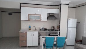A compact kitchen with white cabinets, a gas stove, a sink, and a refrigerator. There is a dining table with two chairs. - Dr.Aslan Apart Hotel - Airport (Cubuk)