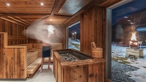A wooden sauna with benches, a fire pit, and a view of a snowy outdoor area. - Tuberis Nature & Spa Resort (Tubre)