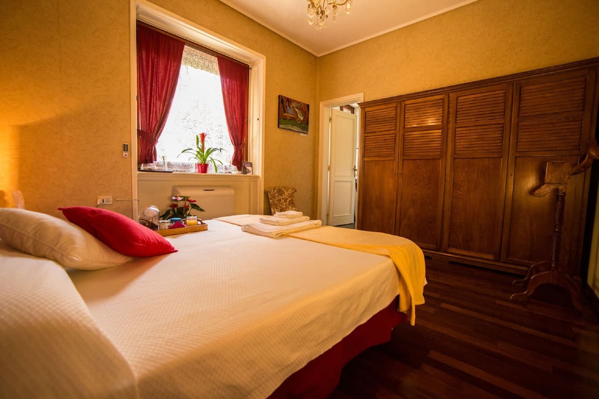 Una habitación de hotel con una cama, un ventanal con cortinas, un armario de madera y una puerta.