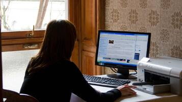 A person seated at a desk with a computer, a printer, and a window with a view of trees.