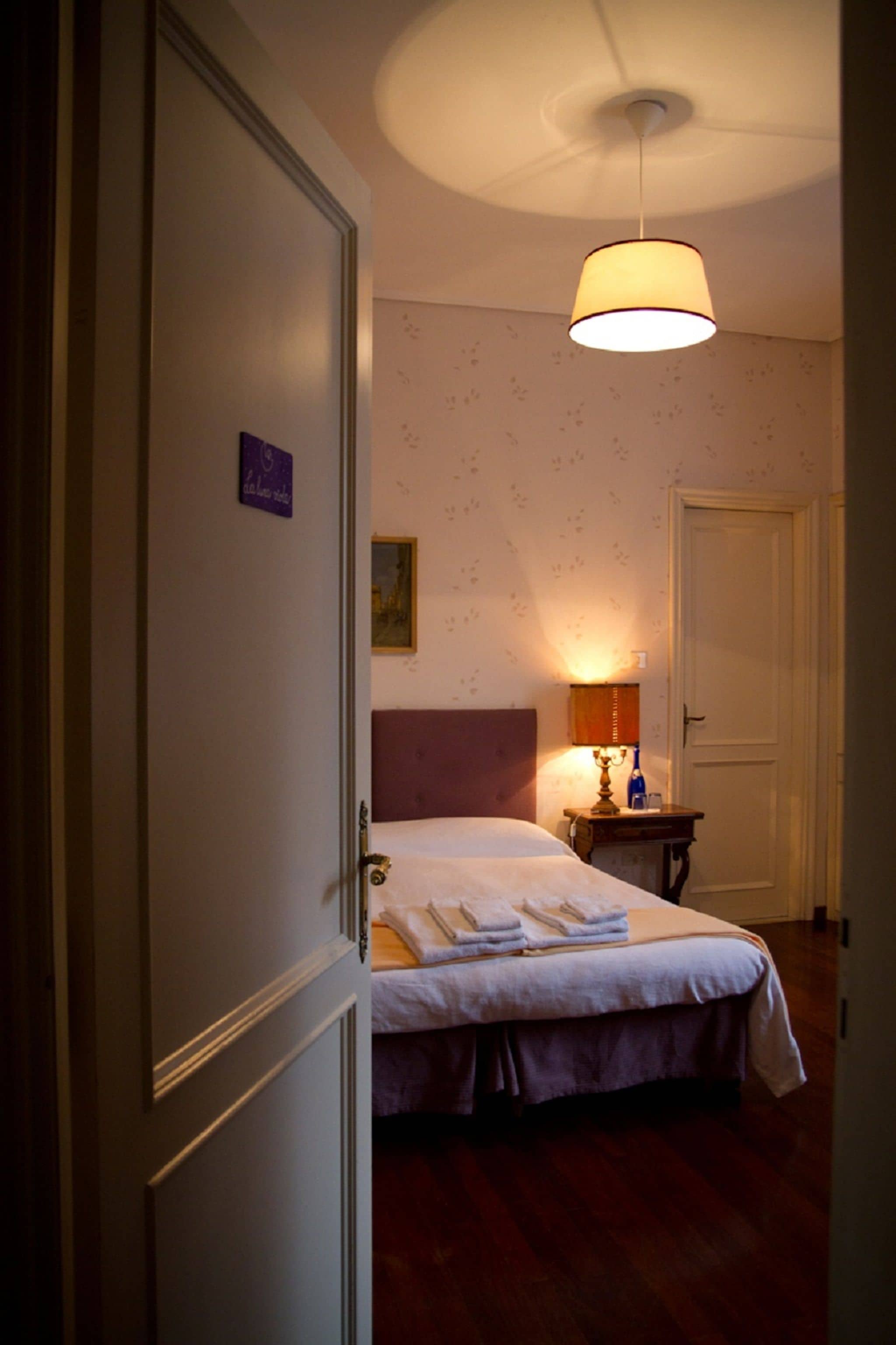 A hotel room with a bed, bedside table, lamp, and a door.