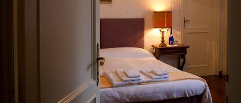 A hotel room with a bed, bedside table, lamp, and a door.
