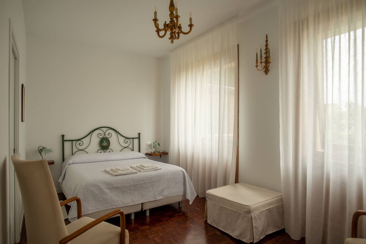 Un dormitorio con cama, una silla, un banco, una mesita de noche y una araña.