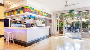 A modern bar area with a colorful mural, a counter with various bottles, and a seating area with outdoor views. - Hotel Cala Murada (Manacor)