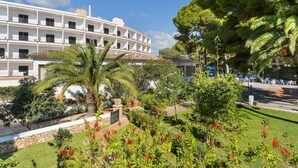 A multi-story hotel with a white facade, a landscaped garden with palm trees, and a pool area. - Hotel Cala Murada (Manacor)