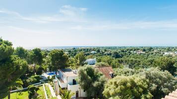 A villa with a swimming pool, surrounded by lush greenery and overlooking a coastal landscape.