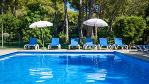 A swimming pool with blue water, surrounded by trees and blue lounge chairs with white umbrellas. - Hotel Cala Murada (Manacor)