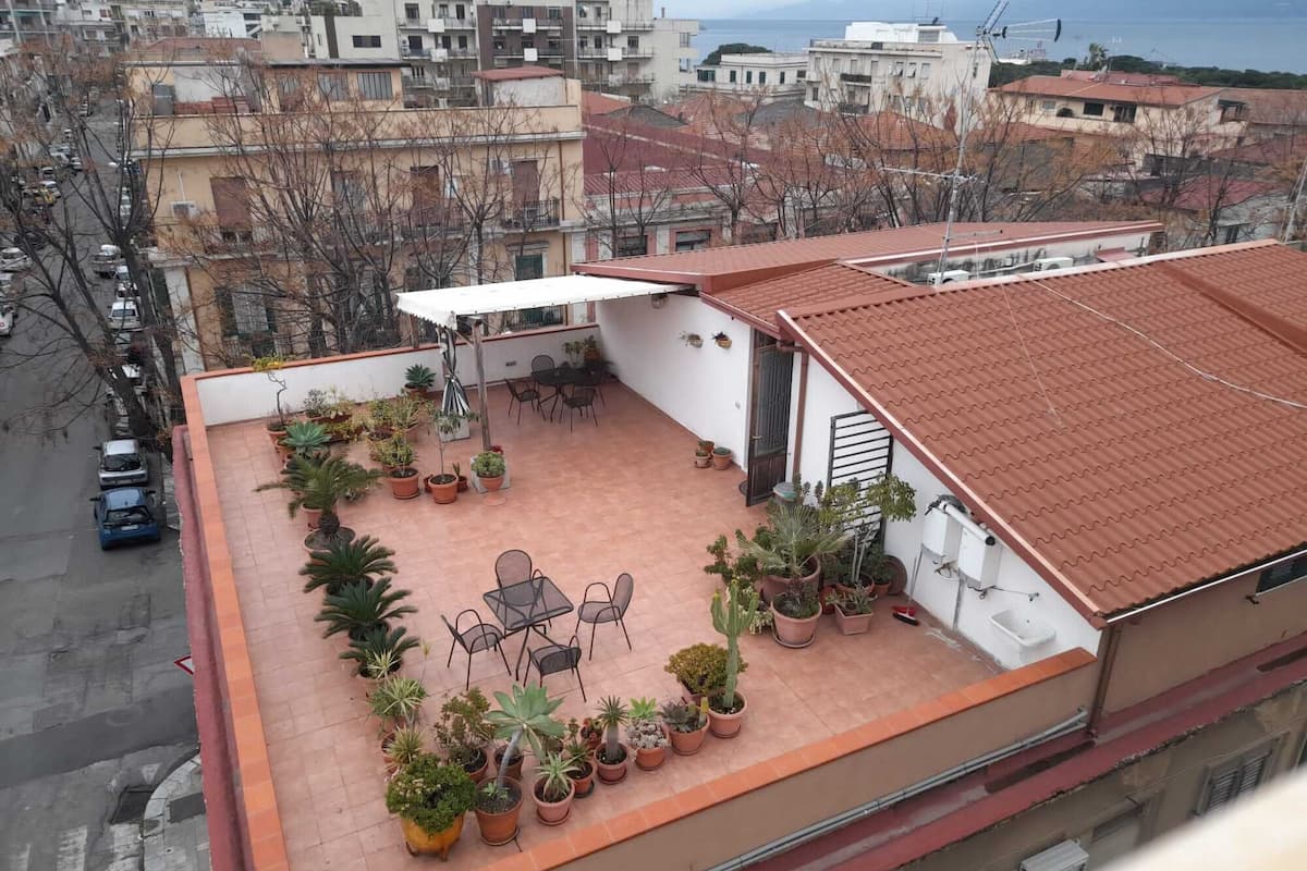 Eine Dachterrasse mit Topfpflanzen, Gartenmöbeln und Blick auf die Stadtlandschaft.