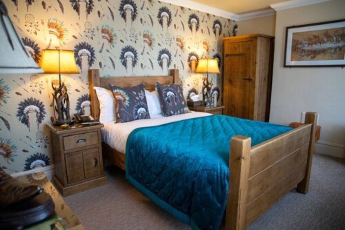 Une chambre à coucher avec un lit en bois, deux tables de chevet, une commode, une armoire et un papier peint à motifs.