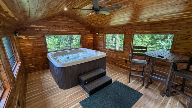 Eine Holzhütte mit Whirlpool, Tisch und Stühlen, sowie großen Fenstern mit Blick auf den Wald.