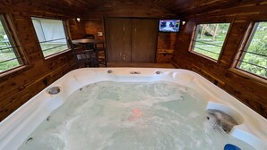 Ein Holzblockhaus-Interieur mit Whirlpool, Fernseher und einer Tür, die nach draußen führt.