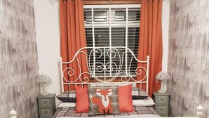 A bedroom with a white metal bed frame, a plaid bedspread, two pillows with a fox design, and orange curtains. - Tarrareoch Farm (Bathgate)