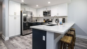 Una cocina moderna con armarios blancos, electrodomésticos de acero inoxidable, una isla grande y taburetes de madera.