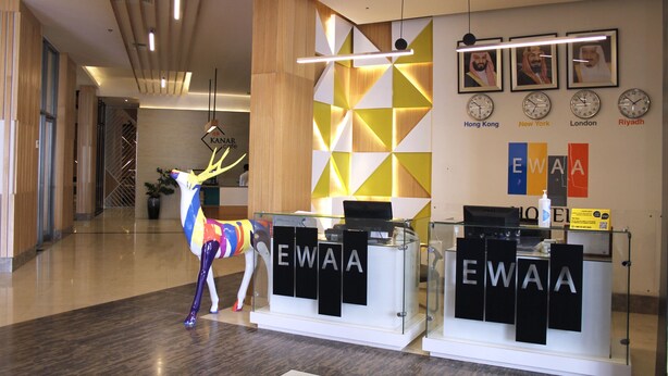 Un área de recepción de diseño moderno, con un escritorio de vidrio, una llamativa escultura de ciervo y relojes mostrando la hora de Hong Kong, Nueva York, Londres y Riad.