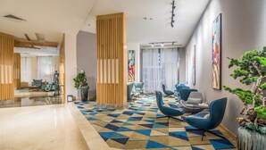 Un vestíbulo moderno con alfombra de diseño geométrico, zona de estar en tonos azules y un mostrador de recepción.