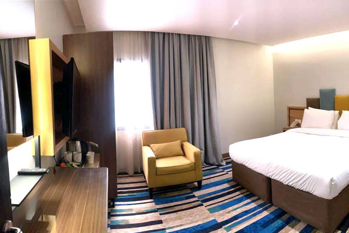 A hotel room with a large bed, a desk, a chair, and a TV.