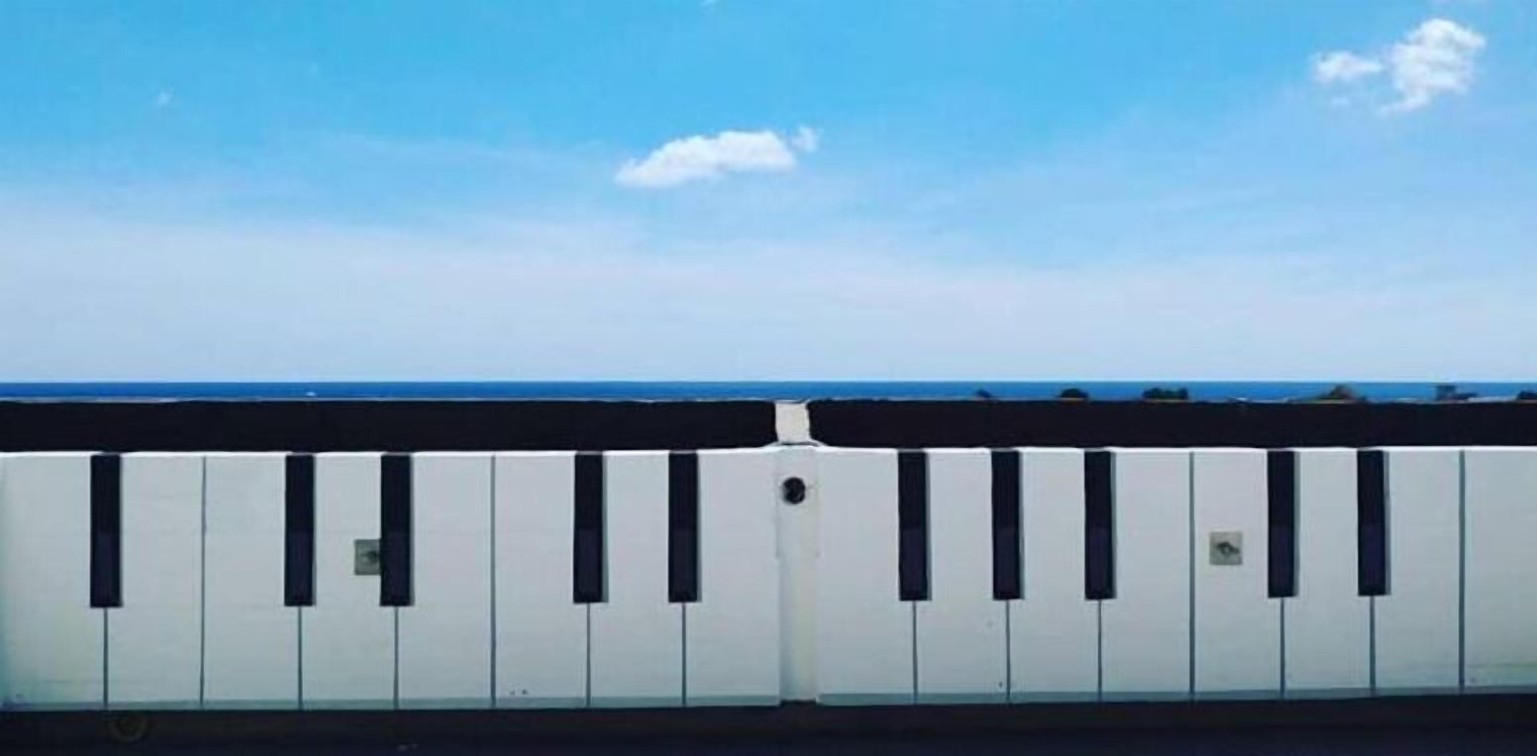 A white fence with black vertical bars, overlooking a body of water under a clear sky.