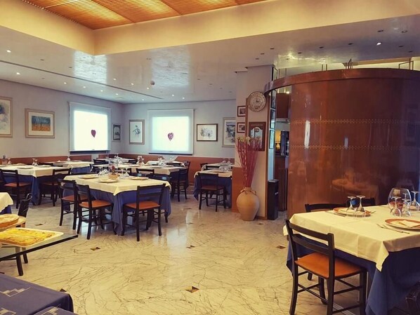 Un restaurante con varias mesas y sillas, una mesa grande en el centro, y un jarrón decorativo.