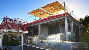 A modern outdoor seating area with a glass enclosure, red railings, and large umbrellas. - Hotel Intervallo (Porto Cesareo)