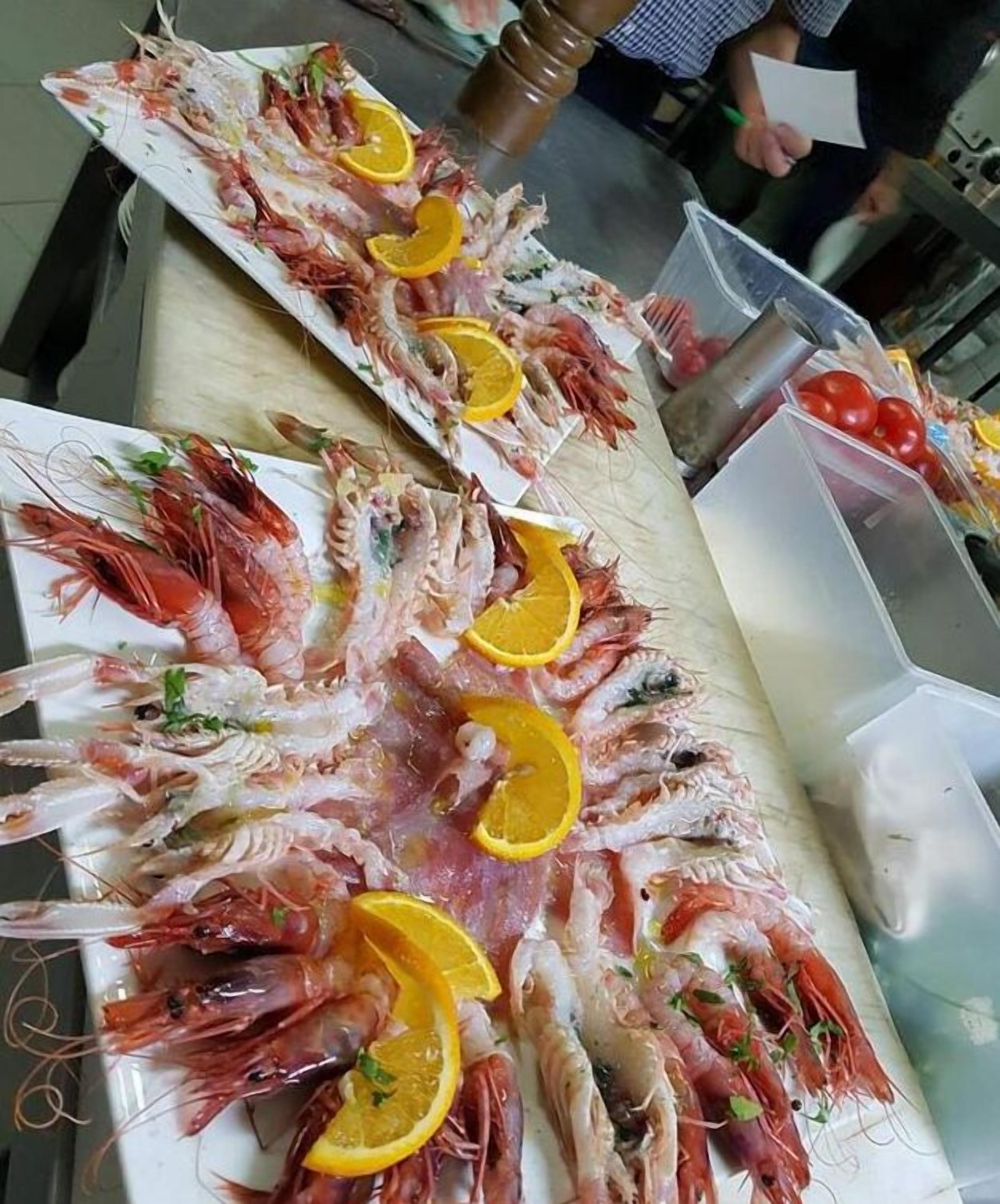 Un plat de marisc amb gambes i rodanxes de taronja damunt un taulell.