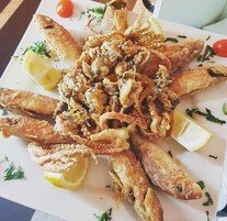 Un plato de mariscos fritos, que incluye camarones y calamares, decorado con gajos de limón y hierbas.