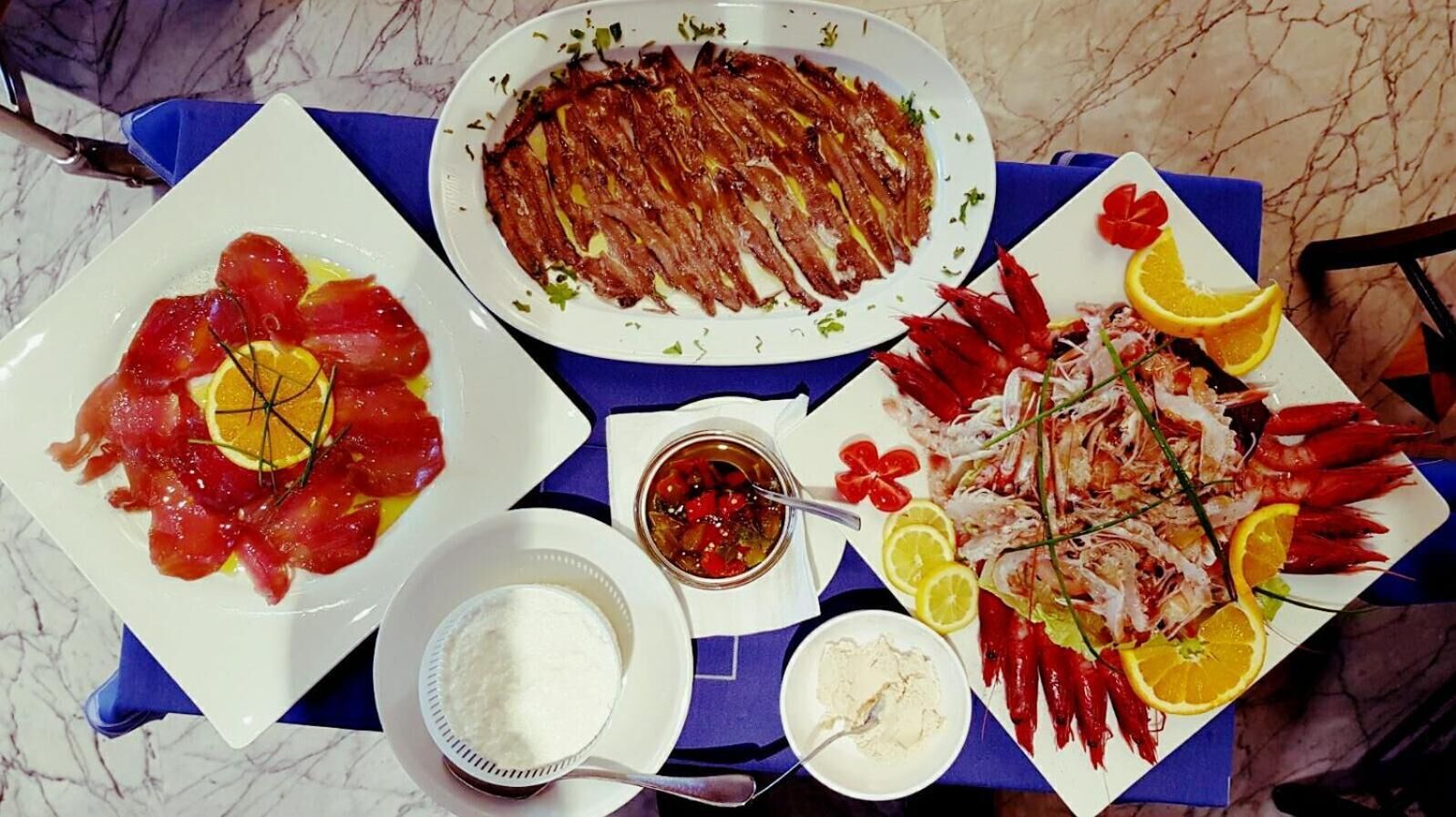 A table with various seafood dishes, including sashimi, shrimp, and a seafood platter, accompanied by lemon slices and a small bowl of sauce.