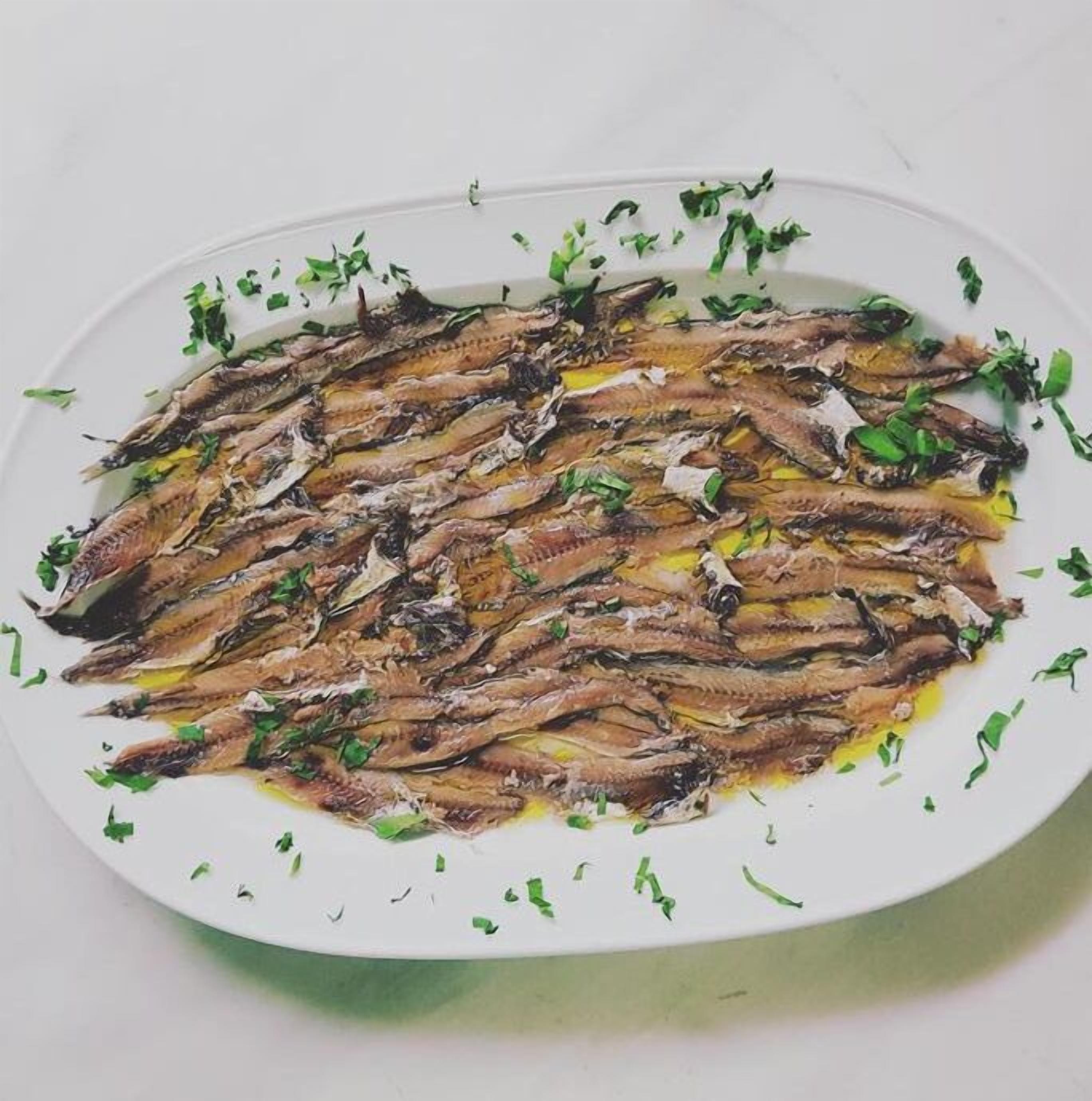 A white oval plate with grilled sardines garnished with chopped herbs.