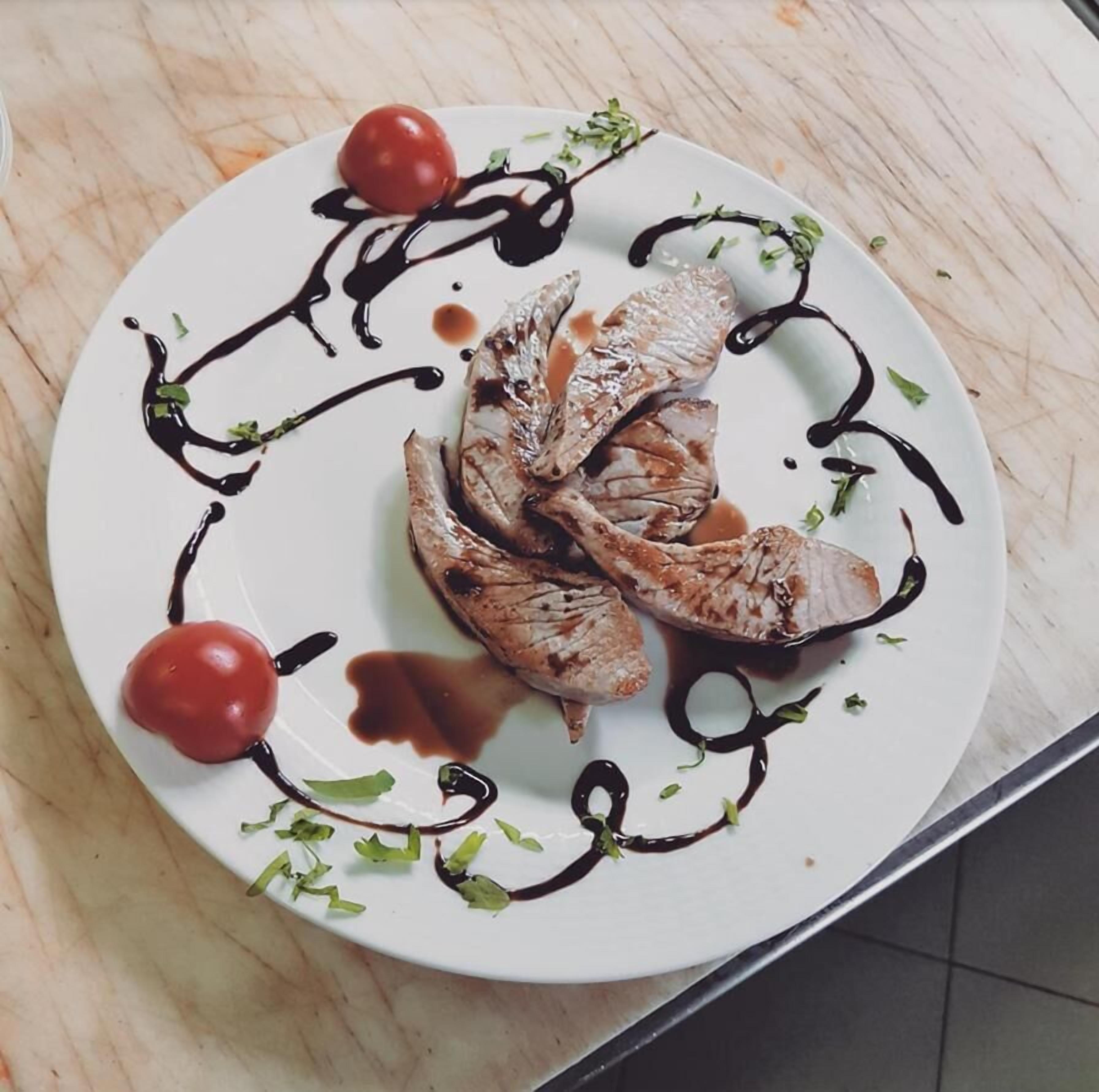 A plate with grilled fish, cherry tomatoes, and a decorative sauce on a white plate.