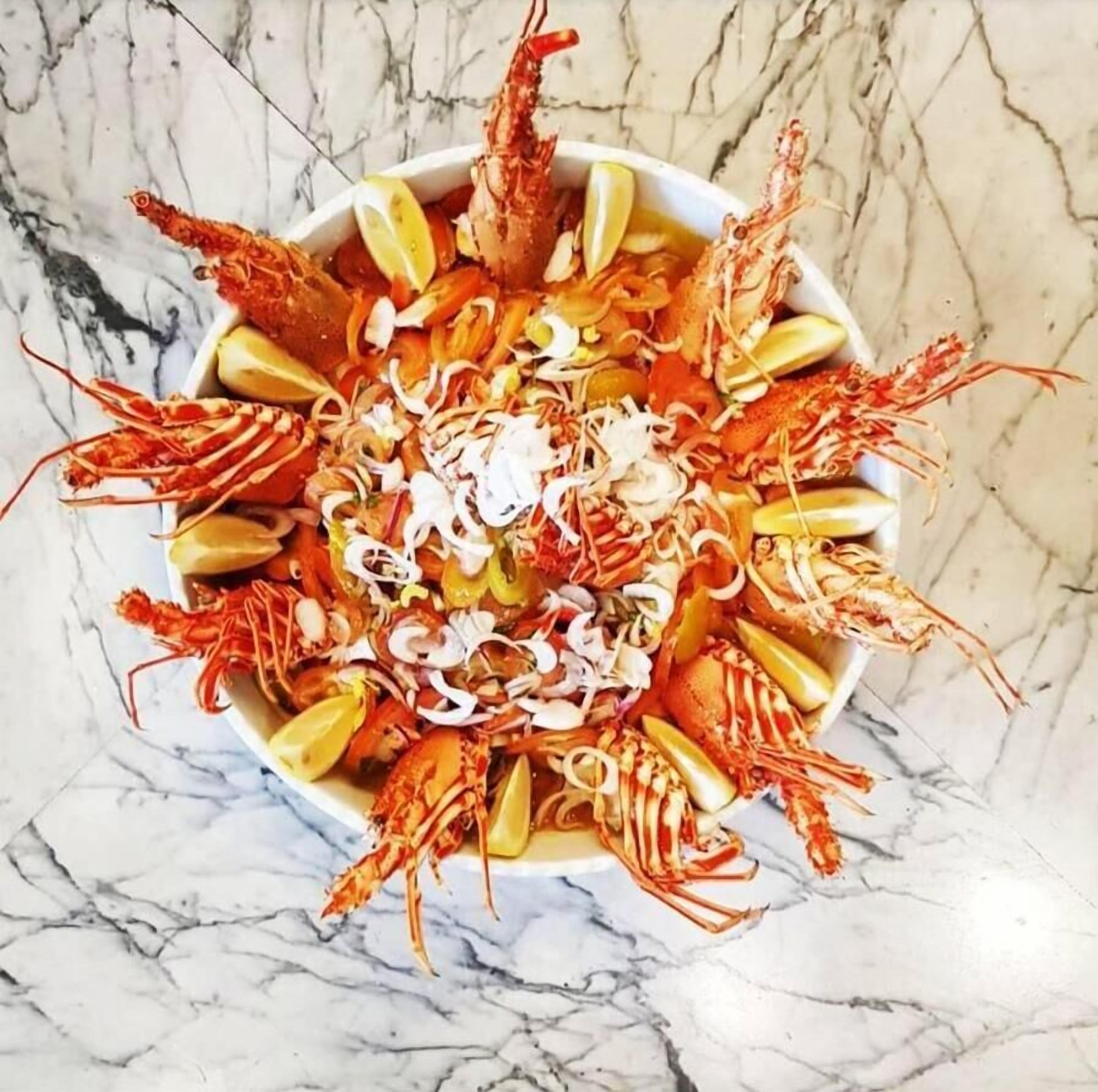 Un plato de langostinos cocidos adornados con rodajas de limón y cebolla picada.