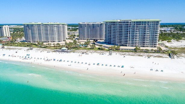 A beachfront hotel with multiple high-rise buildings, a sandy beach, and clear turquoise waters. - Large lobby-level end condo w/patio access to beach & pool! (Destin)