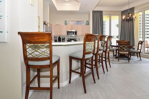 A modern kitchen with a central island, wooden bar stools, and a dining area with a view of the city.