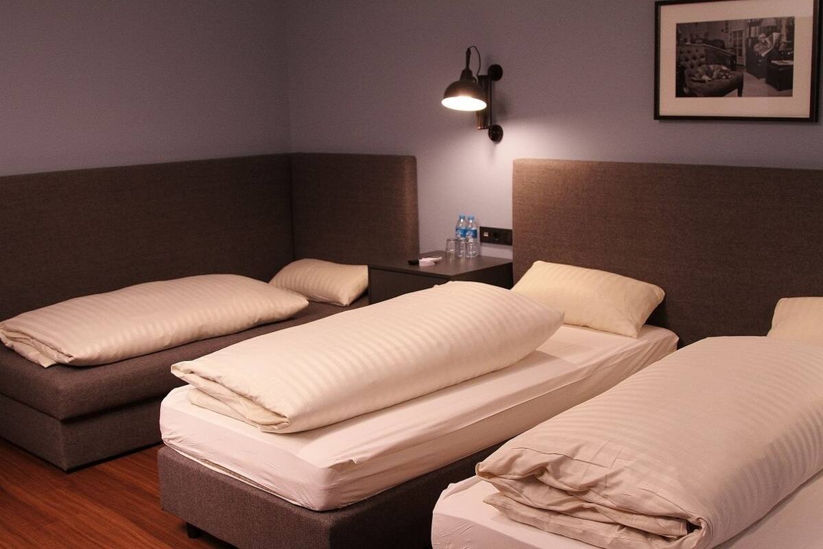 Quarto de hotel com duas camas de solteiro, uma mesinha com abajur e um quadro na parede.