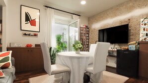 A modern living room with a dining table, white chairs, a flat-screen TV, a bookshelf, and a window with curtains. - Qaral Bed and Breakfast (Cagliari)