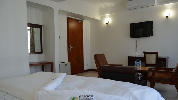 A hotel room with a bed, a desk, a chair, a television, and a door. - Florida Executive Inn (Dar es Salaam)