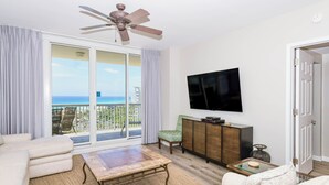 Ein Wohnzimmer mit Sofa, Couchtisch, Fernseher, Deckenventilator, einer Glastür zu einem Balkon und einem Schrank.