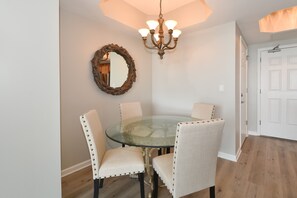 A dining area with a glass table surrounded by four upholstered chairs, a wooden mirror, and a chandelier. - 2BR/2BA Condo Steps from the Beach in Destin (Destin)