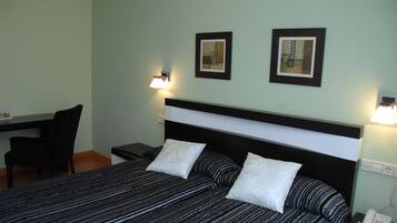 A hotel room with a bed, a desk, and two wall-mounted lamps.