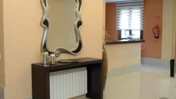 Een hotel receptie met een grote spiegel, een console tafel met decoratieve objecten, een radiator en een brandblusser aan de muur.