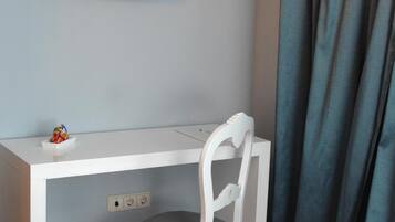A white desk with a television mounted above it, a chair with a cushioned seat, and a power outlet on the desk.