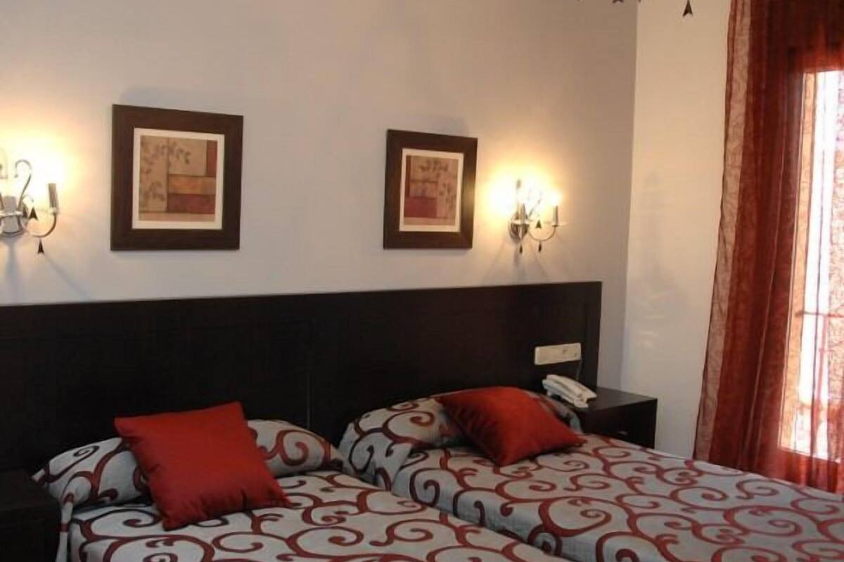 Ein Hotelzimmer mit zwei Betten, jeweils mit rot-weiß gemusterten Bettbezügen, einem dunklen Kopfteil und zwei Wandleuchten.