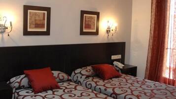 Habitación de hotel con dos camas, cada una con ropa de cama de diseño rojo y blanco, cabecero oscuro y dos lámparas fijadas a la pared.