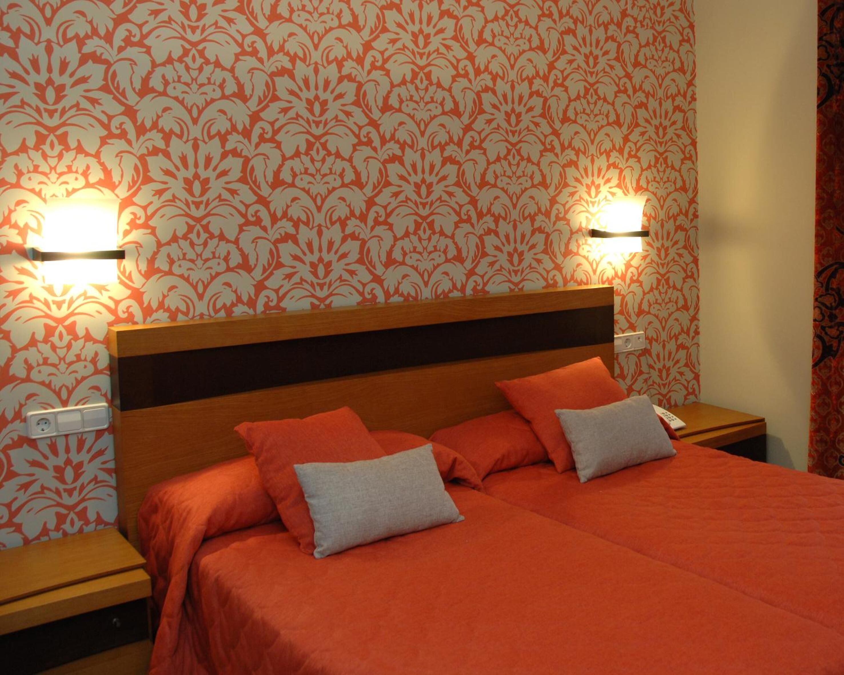 A hotel room with a wooden headboard, two bedside tables, and a bed with orange bedding and pillows.