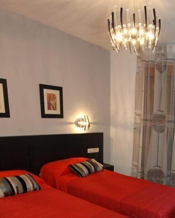 Une chambre d’hôtel avec deux lits, un lustre moderne et des œuvres d’art accrochées aux murs.