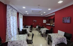 Comedor con mesas y sillas, paredes rojas e iluminación en el techo.