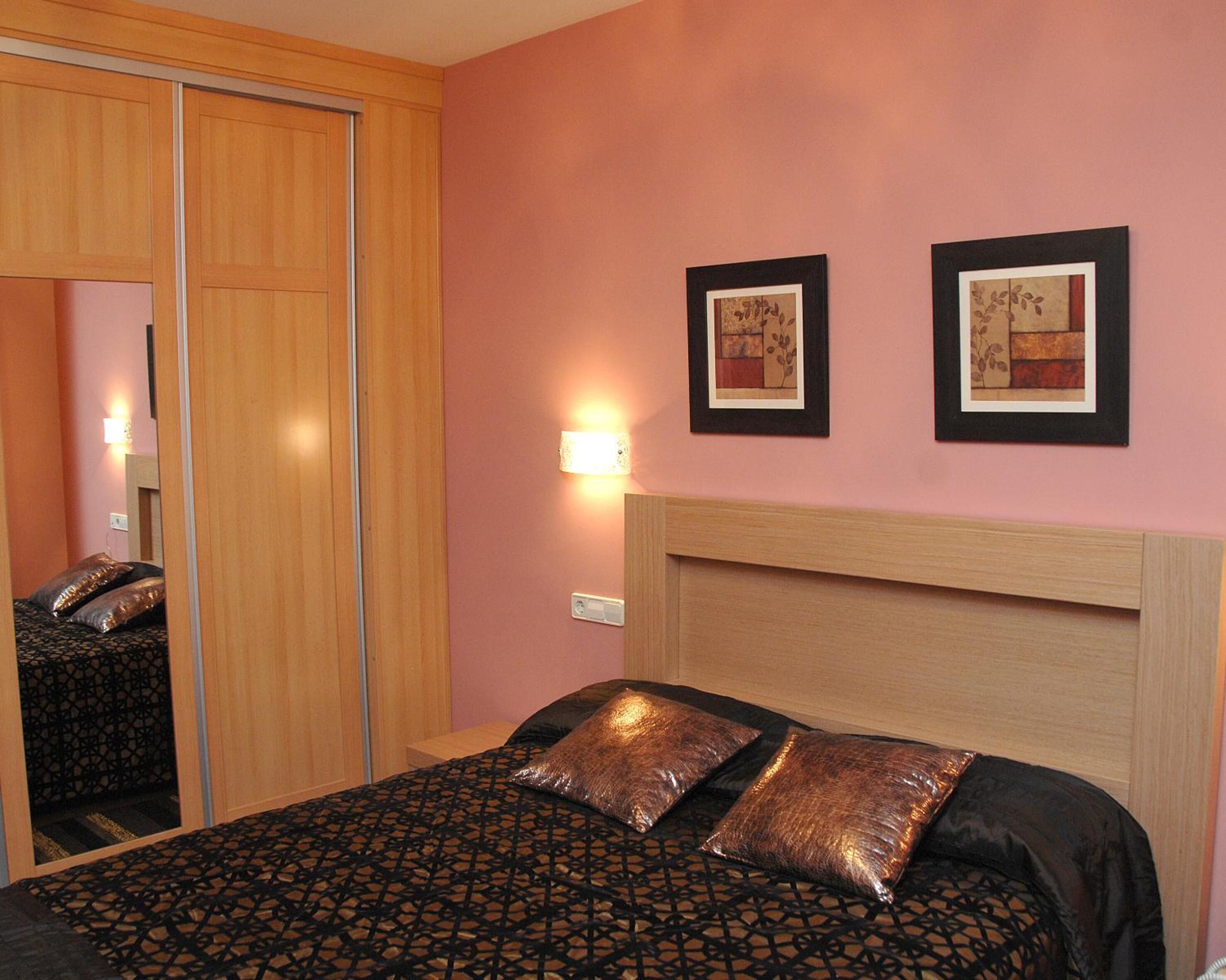 Una camera d'albergo con un letto, una testiera in legno, un comodino, una lampada a parete e due quadri incorniciati.