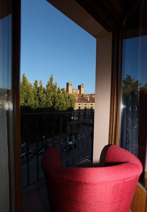 A balcony with a red chair, a glass railing, and a view of buildings and trees.