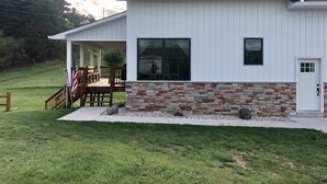 Uma casa moderna de dois andares com varanda coberta, alicerce de pedra e gramado bem cuidado.